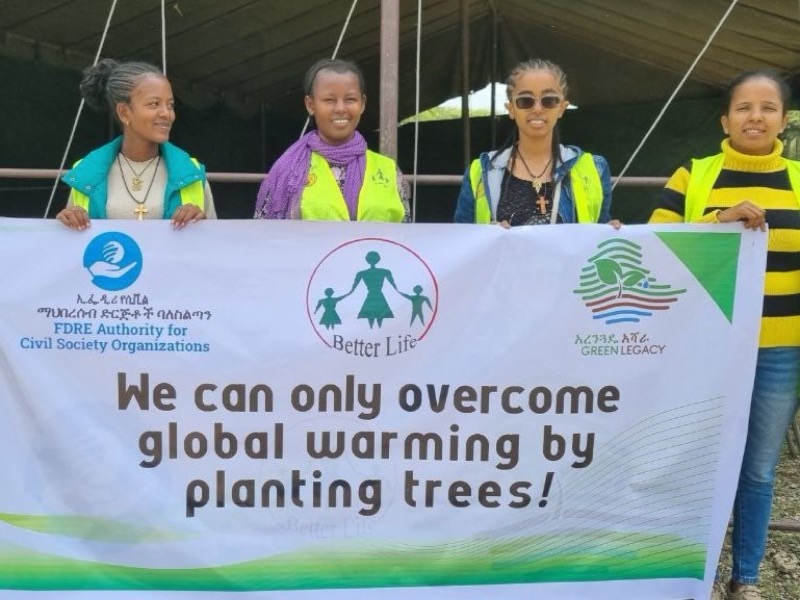 Des jeunes en gilets tiennent une banderole « We can only overcome global warming by planting trees! ».